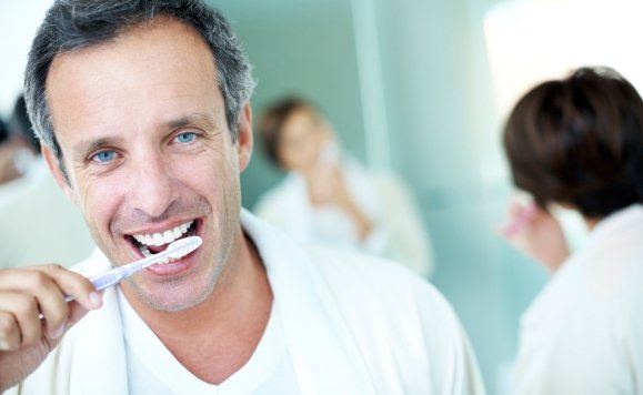 Man with dental implant supported replacement tooth brushing teeth