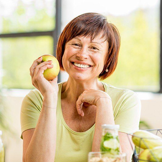 Smiling woman holding an apple after dental implant tooth replacement