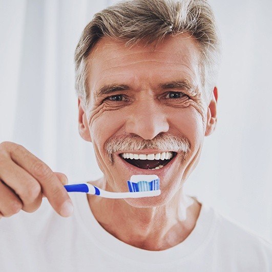 Man brushing teeth after dental implant tooth replacement