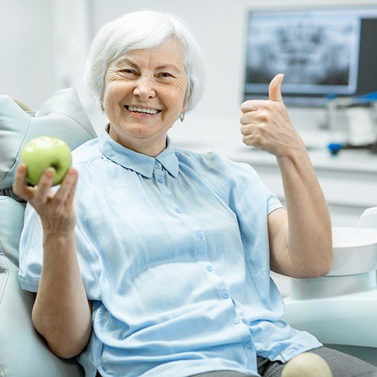 Smiling woman in dental chair holding an apple