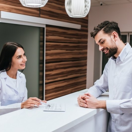 dental assistant at front desk talking with patient about dental implant financing options