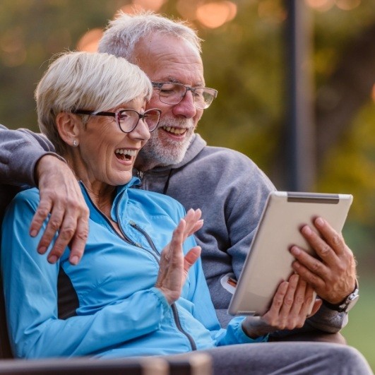senior woman and man couple looking on ipad for affordable dental implants