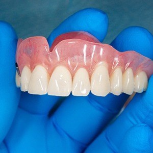 Close-up of gloved hand holding full denture for upper arch
