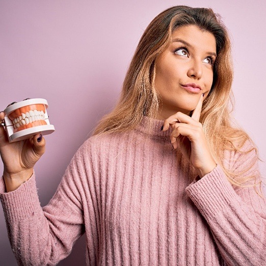 Young woman with questions about dentures, holding dental model