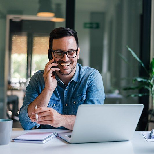 Smiling man talking on phone and looking at laptop