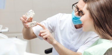 Dentist and patient looking at dnetal implant supported fixed bridge model