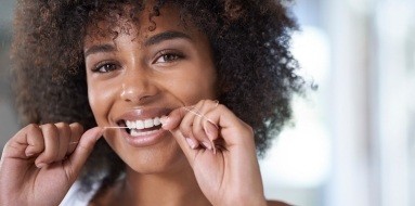 Woman flossing teeth to care for her smile after dental implant tooth replacement