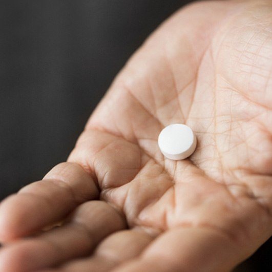 Sedative pill in patient’s hand, set against dark background