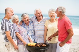Happy seniors eating with dentures at beach barbecue