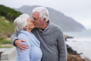 Romantic senior couple standing outside, kissing with dentures