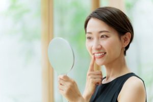 Woman holding hand mirror, admiring her teeth