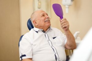 Senior dental patient using mirror to admire his new restorations